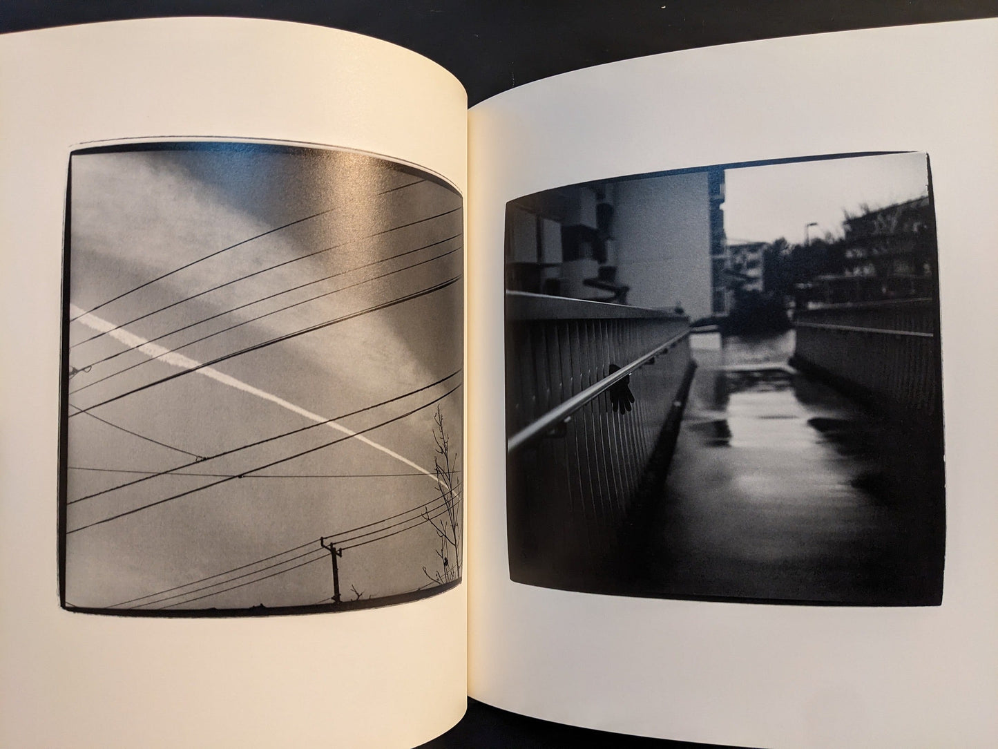 Spread from “Walk while ye have the light” showing intersecting overhead power lines in the sky and a wet bridge with a railing leading into the distance.