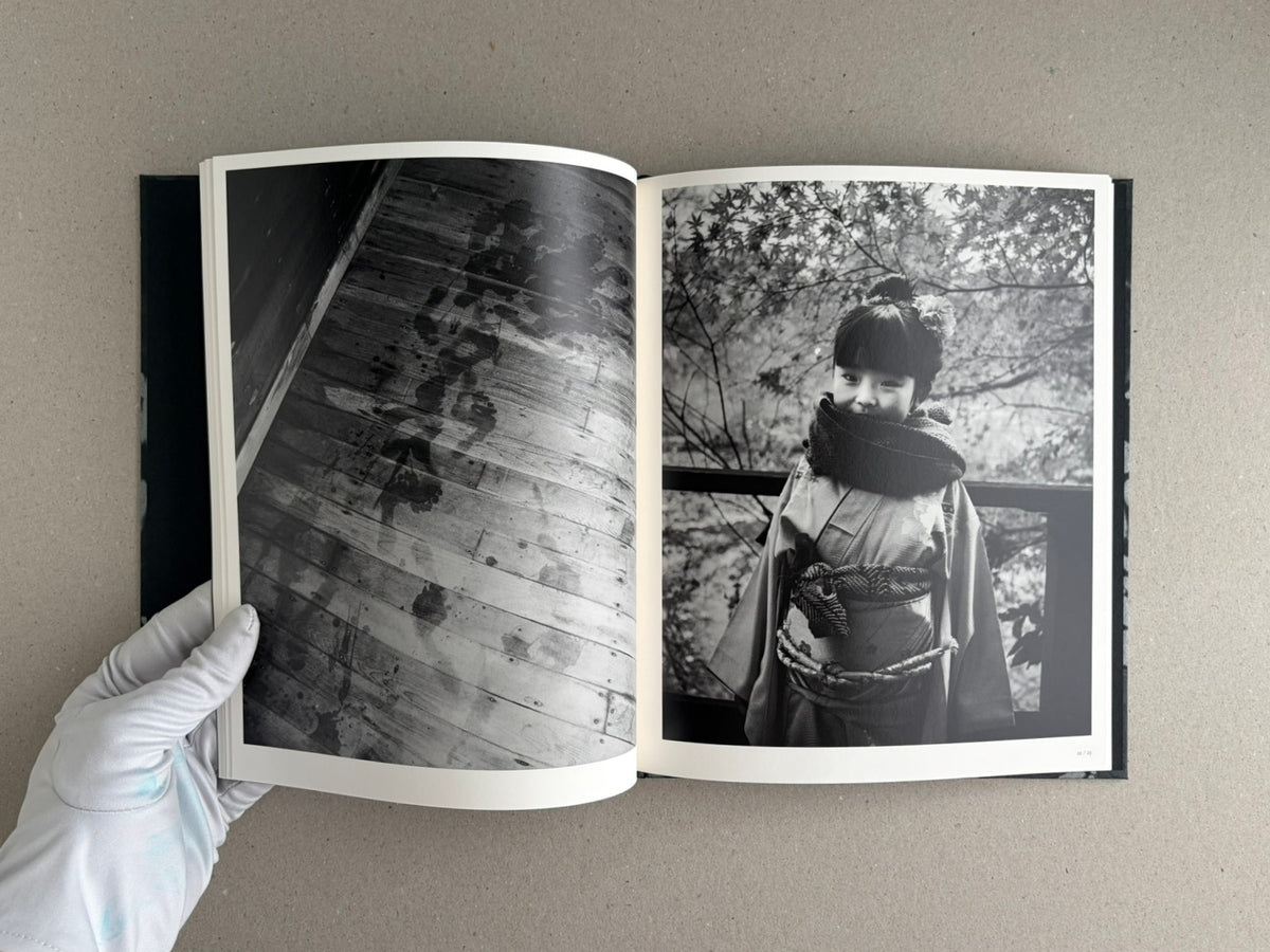 Open photobook Wandering Dog – Mai Nakama showing a black-and-white spread: a dark wooden floor with footprints on the left, and a child in traditional dress on the right.