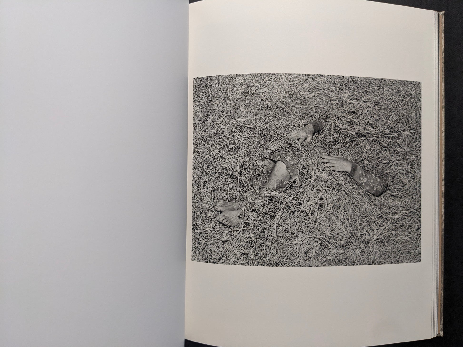 Interior photograph from What the Rain Might Bring — figure partly covered in hay or dry grass, black and white.