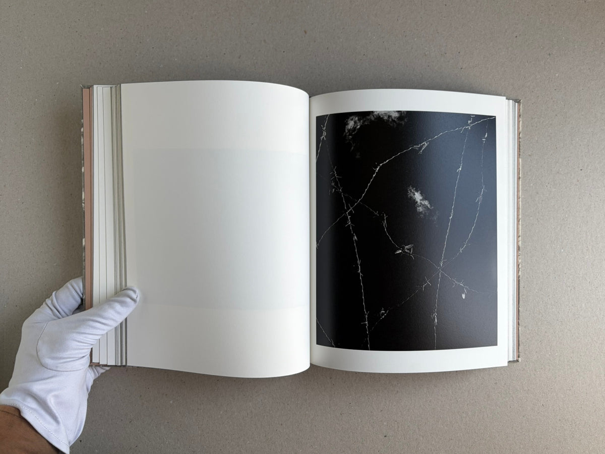 Open photobook What the Rain Might Bring by Dylan Hausthor, showing a blank left page and a black duotone image on the right page, held open by a gloved hand.