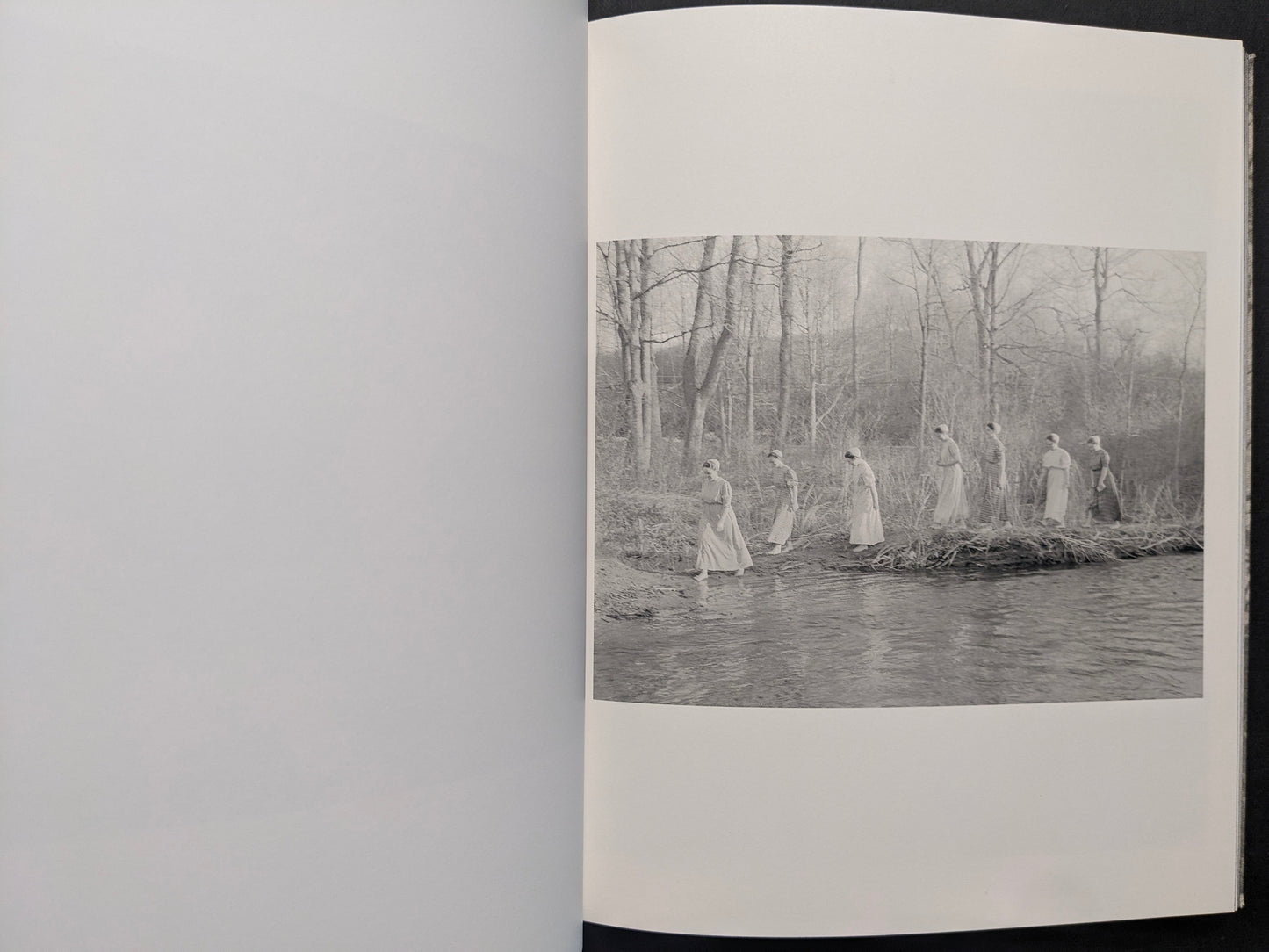 Interior photograph from What the Rain Might Bring — a line of figures walking through shallow water, black and white.