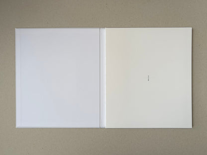 Open Yamamoto Masao photobook showing blank white endpapers and a small vertical Japanese title mark on the right page.