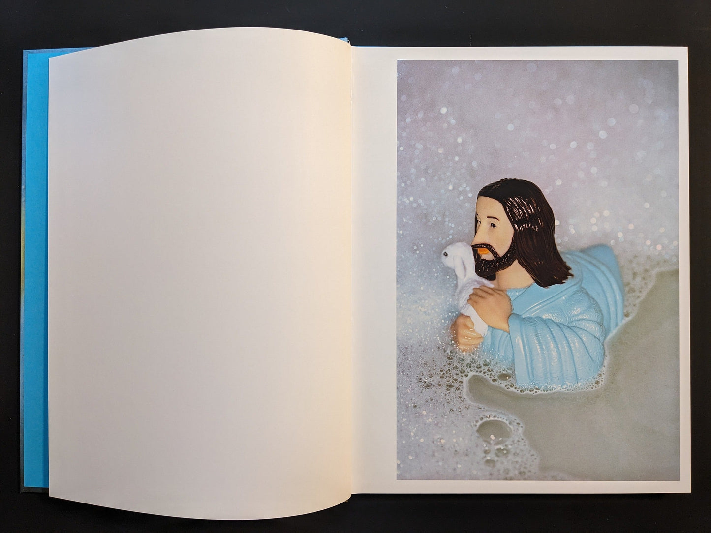 Inside page from “¥€$U$ (JESUS)” of a plastic Jesus figure holding a lamb, floating in a bathtub filled with foam.