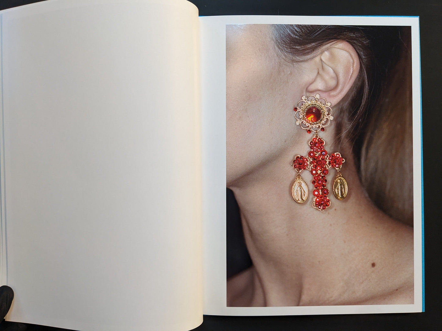 Inside page from “¥€$U$ (JESUS)” with a close-up of a person’s ear wearing a large red cross earring with small saint medallions.